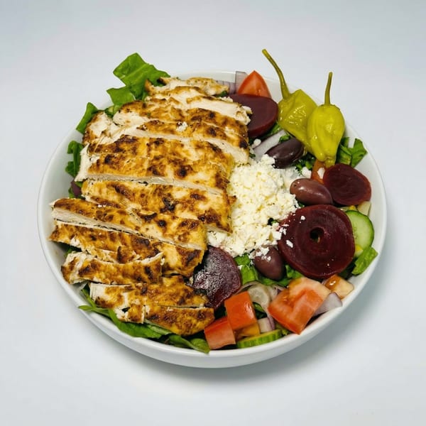A vibrant salad with grilled chicken, feta, olives, beets, tomatoes, cucumbers, and peppers in a white bowl.