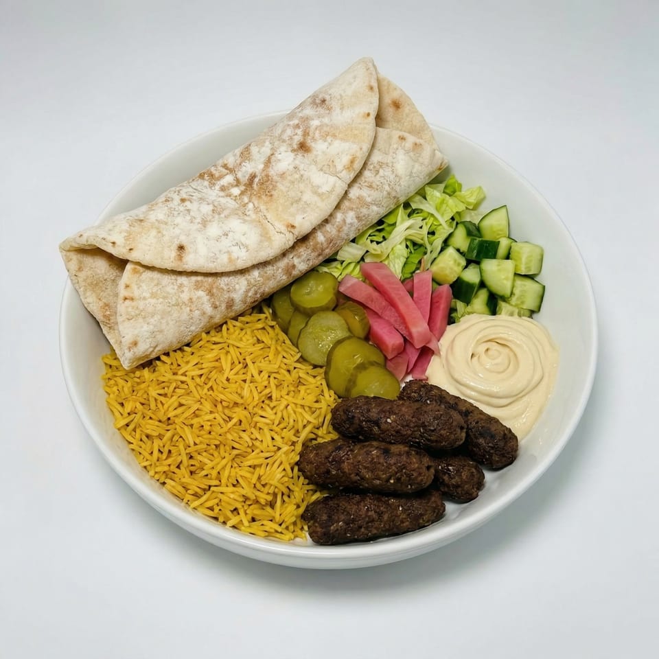 A white bowl filled with yellow rice, kebab, hummus, pita bread, pickles, and salad.