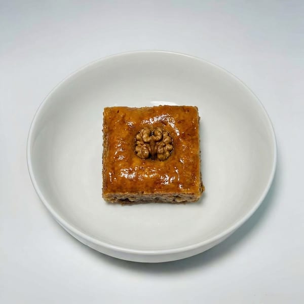 A single square piece of baklava, topped with a walnut, sits in a white bowl.